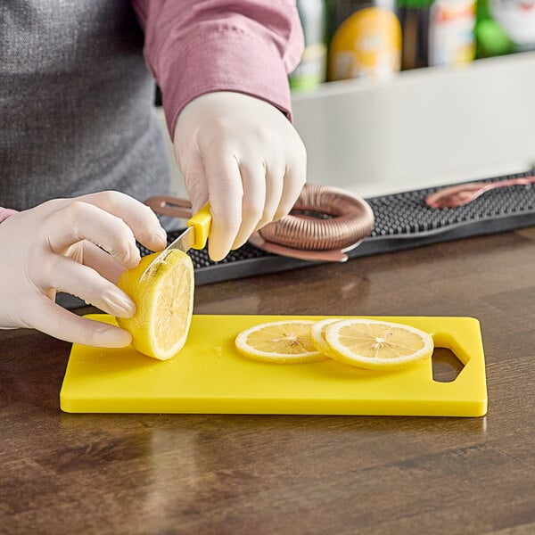 A person wearing gloves uses a yellow Choice polyethylene cutting board to cut lemons.