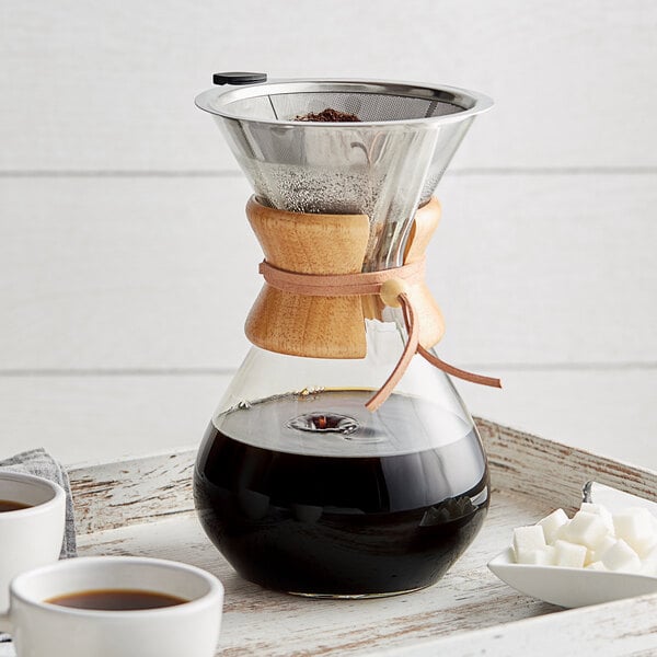 An Acopa glass pour over coffee maker with wood collar over a cup of coffee.