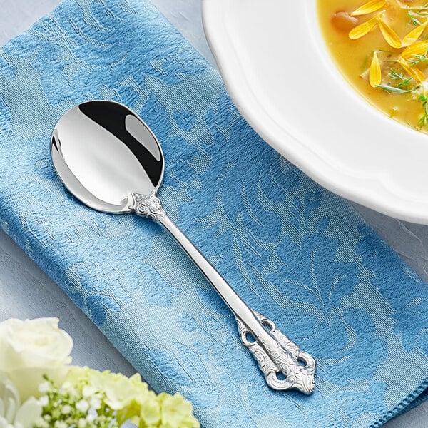 An Acopa stainless steel bouillon spoon with a silver handle on a blue napkin.