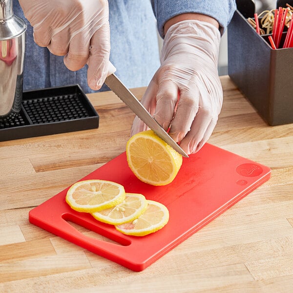 A person slicing a lemon on a red Choice polyethylene cutting board.