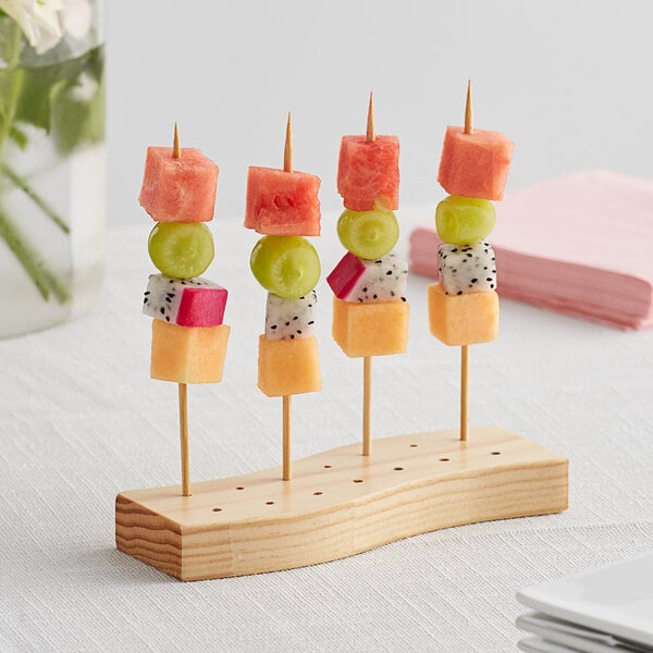 A wooden Acopa Mesa skewer holder with fruit on sticks.