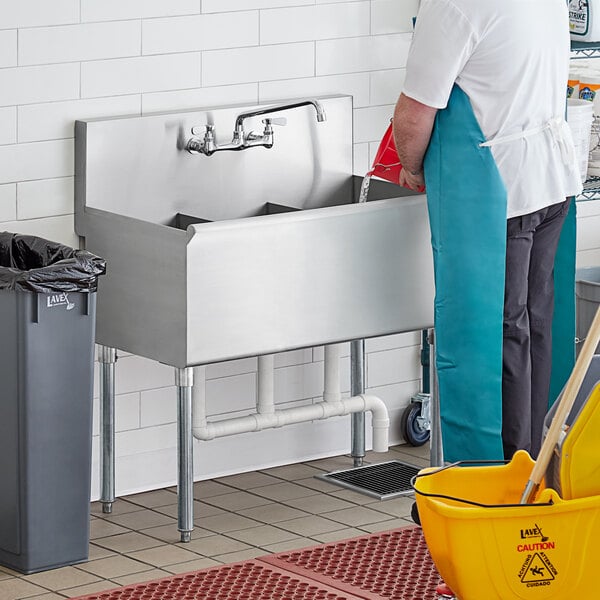 A man in a blue uniform washing a Regency stainless steel utility sink.