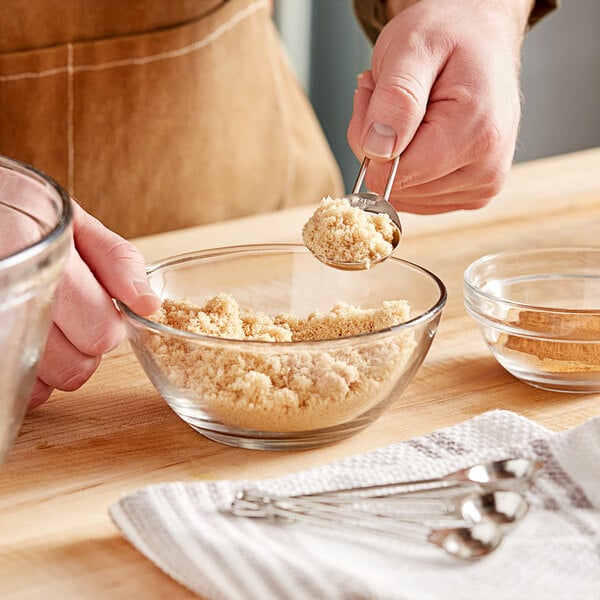 A person using Choice stainless steel measuring spoons to pour brown powder into a bowl.