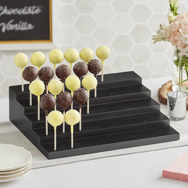 An Acopa black wood skewer and cake pop holder with chocolate and yellow cake pops displayed on a table.