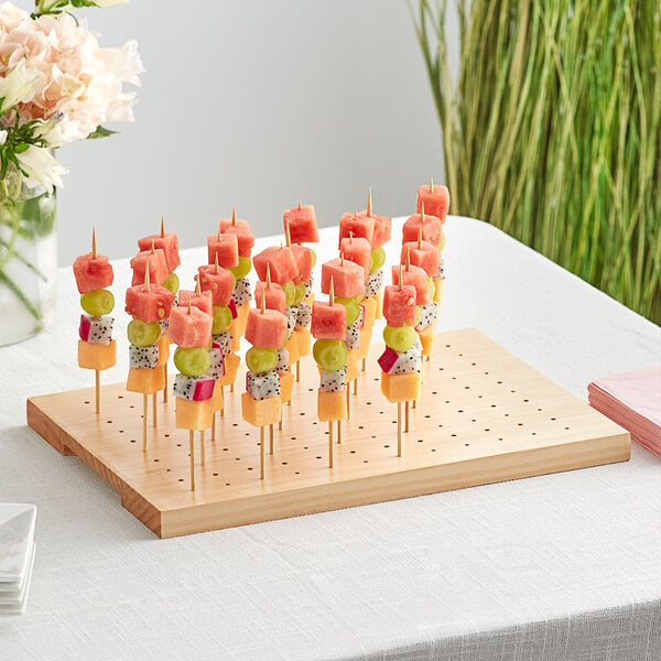 An Acopa natural wood skewer holder with fruit on it.