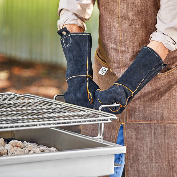 A man wearing Mr. Bar-B-Q leather gloves standing over a grill.