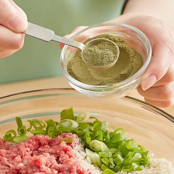 A hand holding a spoon over a bowl of Regal Ground Parsley Leaves.