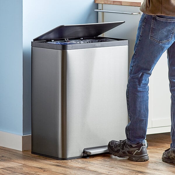 A person using a Rubbermaid metal dual stream step-on trash can.