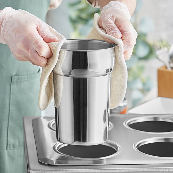 A person wearing gloves and cleaning a stainless steel vegetable inset.