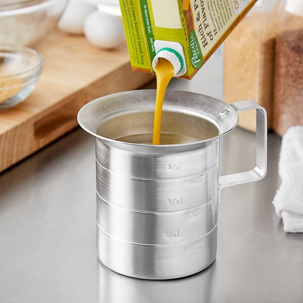 A metal Choice measuring cup with liquid being poured from a carton.