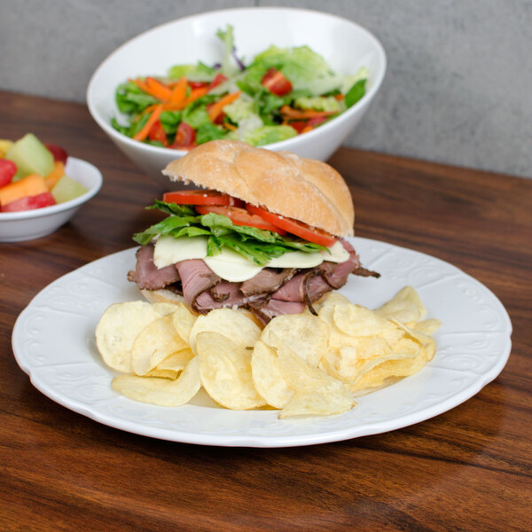 A Tuxton Chicago bright white china plate with a sandwich, chips, and salad.