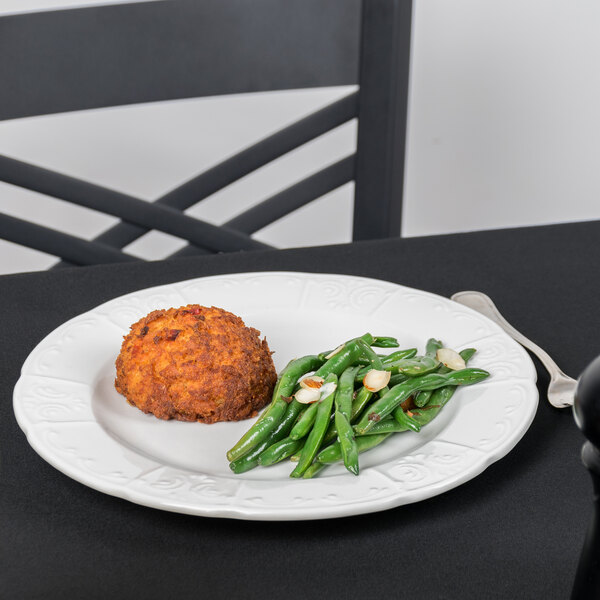 A Tuxton Chicago bright white china plate with meat and green beans on it on a table.