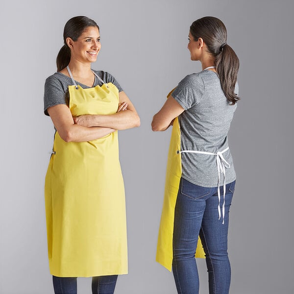 Two women wearing Choice yellow vinyl aprons standing in a professional kitchen.