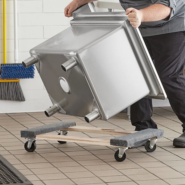 A man pushing a large metal container on a Lavex wood dolly with carpeted ends.