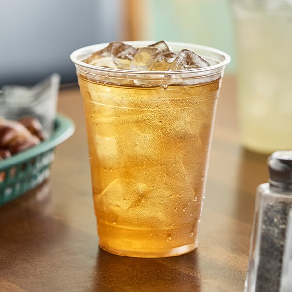 A clear Dart Polypropylene cup filled with ice and iced tea on a table.