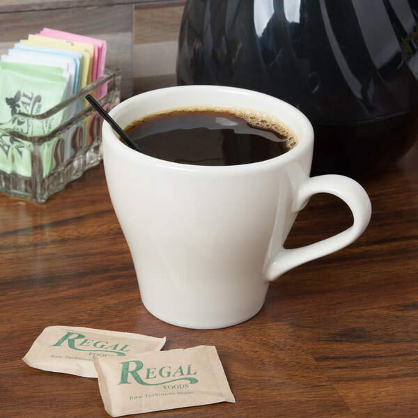 A white Tuxton Europa cappuccino mug filled with coffee on a table with a black straw.