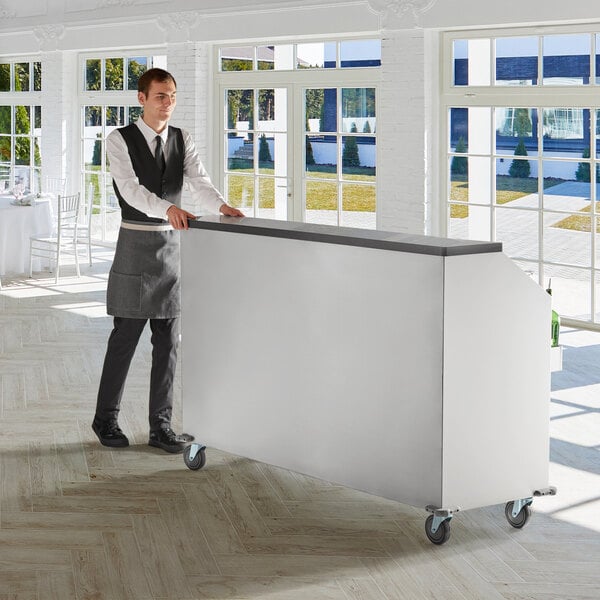 A man standing behind a white Regency portable bar with a stainless steel top.