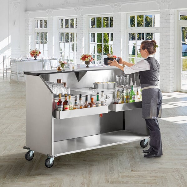 A woman standing behind a Regency portable bar with bottles and glasses.
