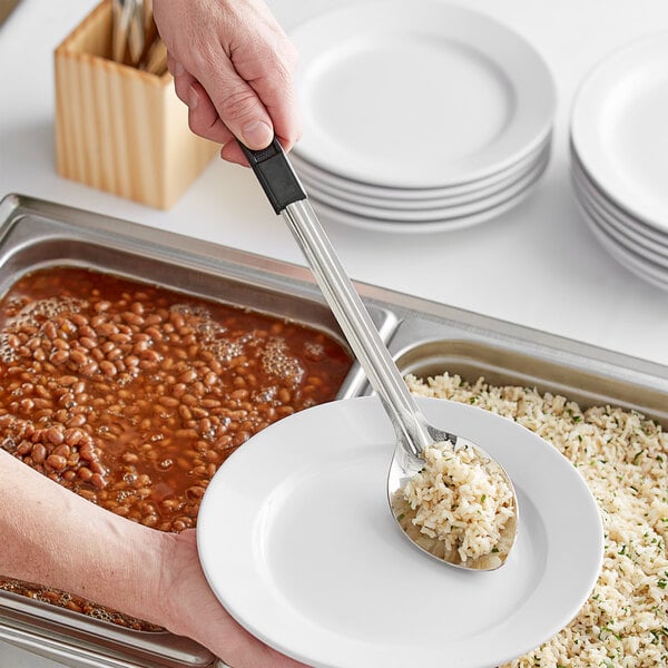 A person using a Choice stainless steel basting spoon with a black handle to serve food on a plate.