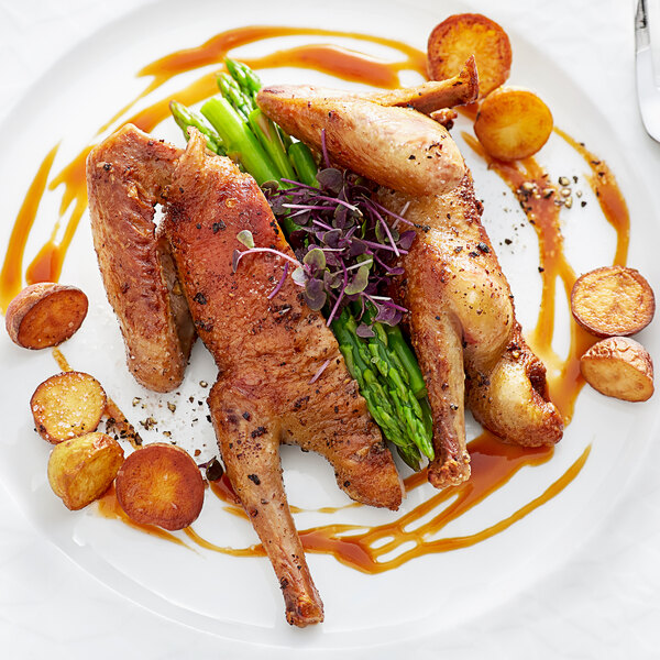 A plate of Squab with vegetables and a fork and knife.