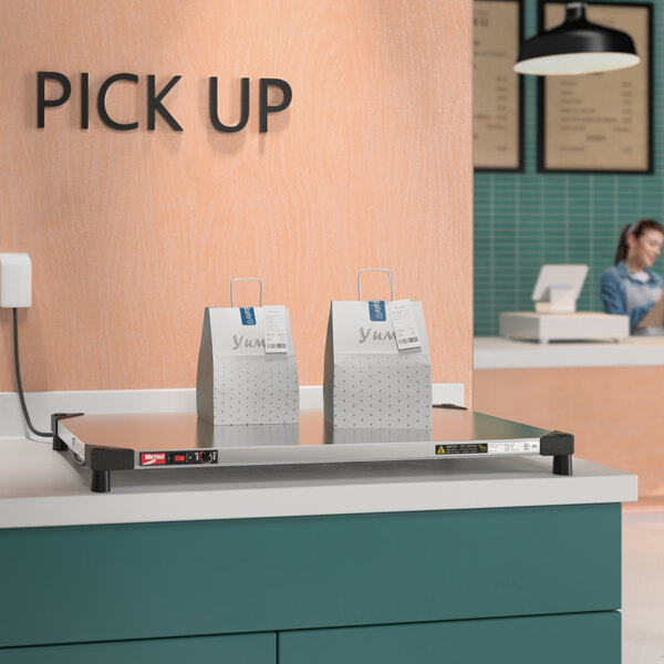 A Metro Super Erecta stainless steel countertop shelf warmer on a counter with a couple of bags on it.