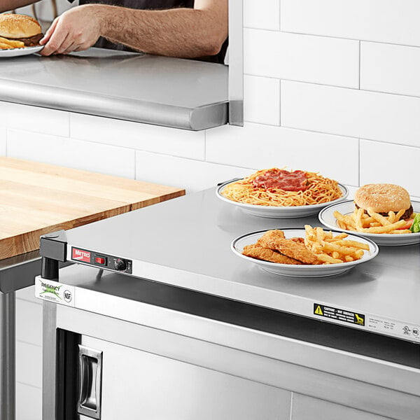 A man using a Metro stainless steel countertop shelf to keep a plate of burger and fries warm.