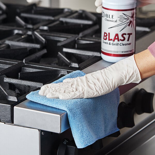 A person in gloves using Noble Chemical Blast oven and grill cleaner to clean a stove.