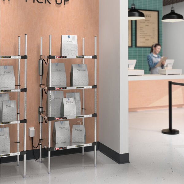 A woman standing in front of a Metro heated stainless steel takeout station with bags on the shelves.