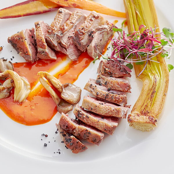 A white plate with a Squab Producers of California boneless squab breast and vegetables.