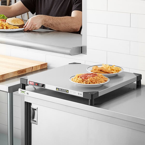 A man using a Metro stainless steel countertop shelf warmer to keep plates of spaghetti and fries warm.