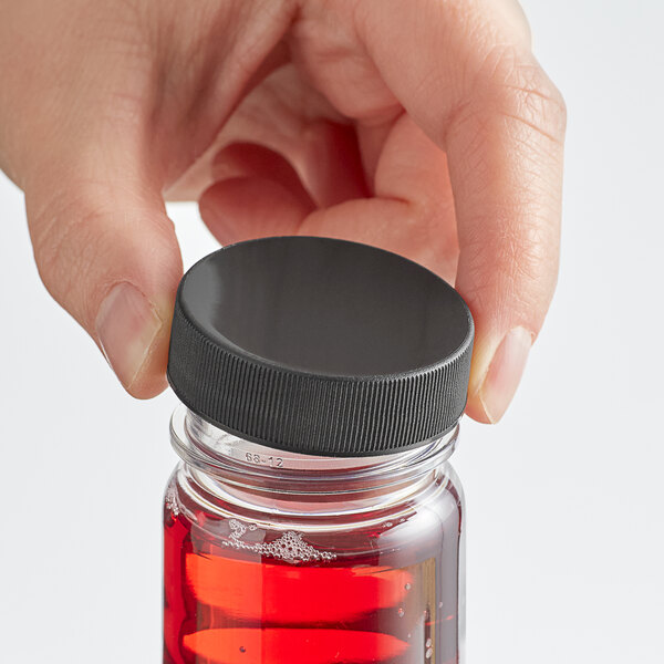 A person's hand holding a black bottle of red liquid with a 38/400 black ribbed cap.