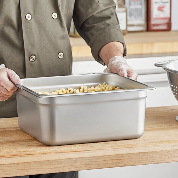 A man in a chef's uniform preparing pasta in a Choice stainless steel steam table pan.