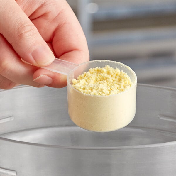 A hand holding a yellow measuring spoon with a yellow powder.