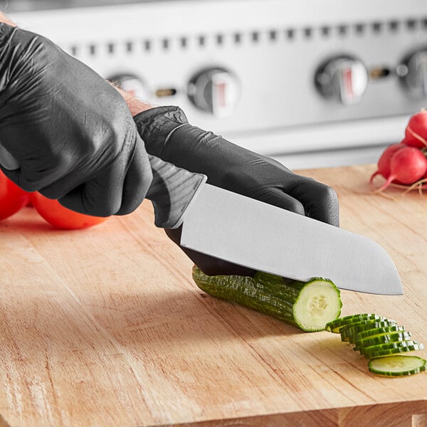A person wearing black gloves uses a Schraf Santoku knife to cut a cucumber.
