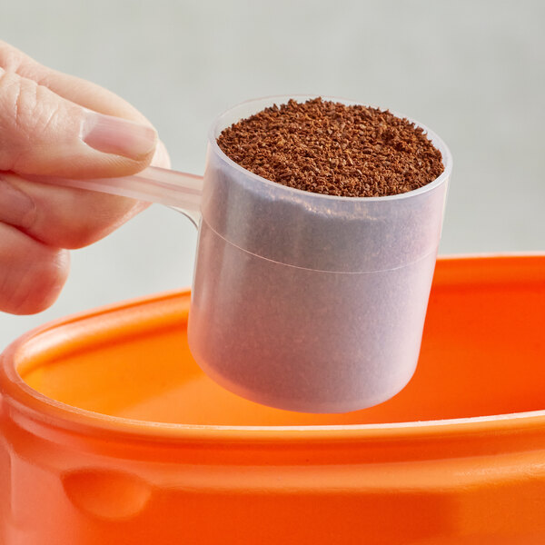 A hand using a small polypropylene scoop to fill a container with coffee powder.