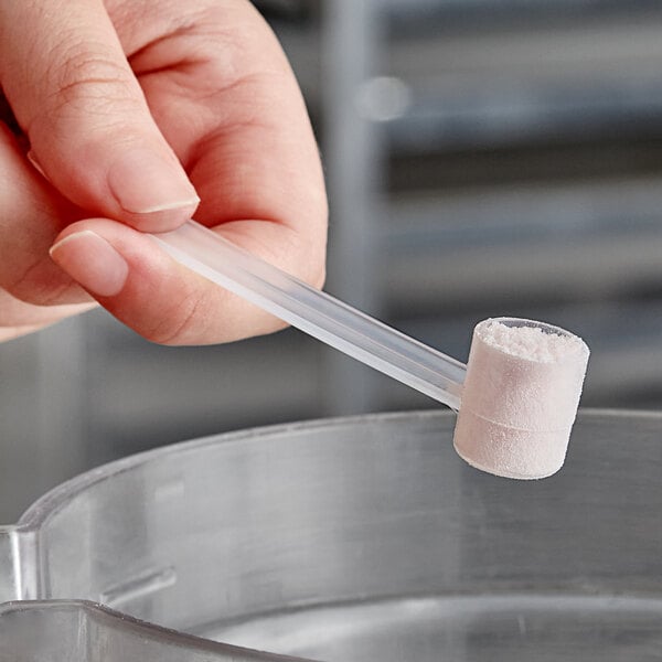 A person holding a 2.5 cc polypropylene scoop with a white powder inside a plastic tube.