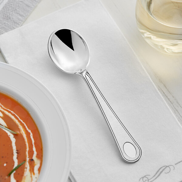 A Visions heavy weight silver plastic soup spoon on a white napkin next to a bowl of soup.