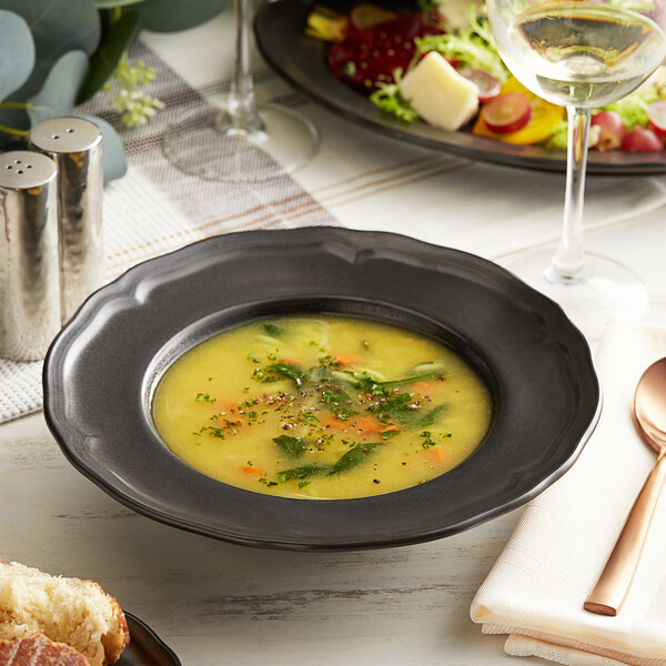 An Acopa Armor Gray porcelain bowl of soup and a wide rim with a spoon next to a plate of bread.