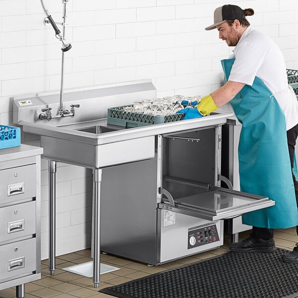 A man in a blue apron washing dishes in a Regency stainless steel dishtable.