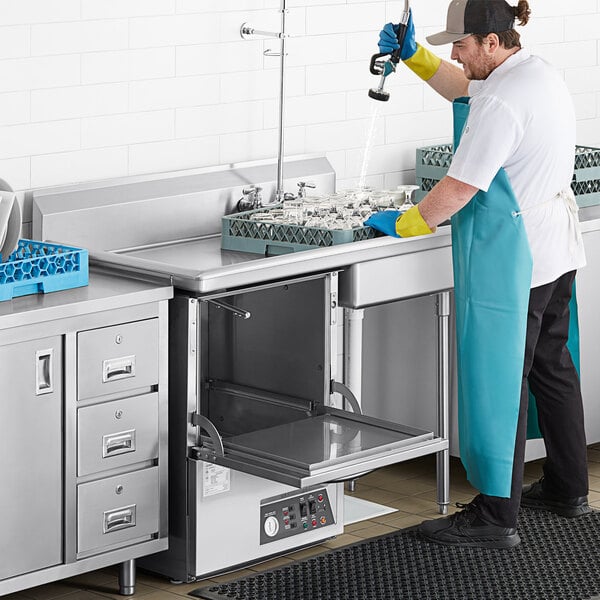 A man in a blue apron washing dishes on a Regency stainless steel dishtable.