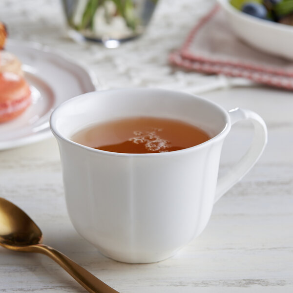 An Acopa white porcelain cup with a gold spoon next to a cup of tea on a table.