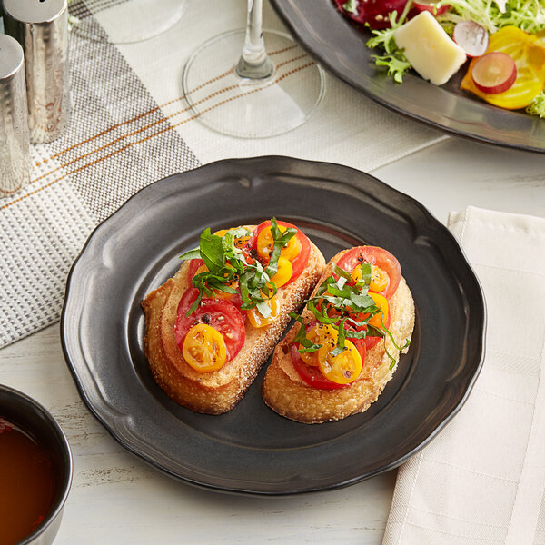 An Acopa Condesa armor gray porcelain plate with bread, tomatoes, and salad on a table.