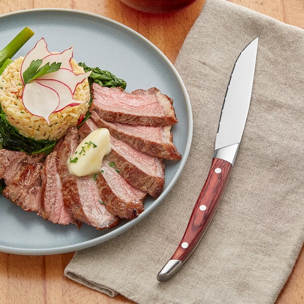 An Acopa steak knife next to a plate of meat and rice with vegetables.