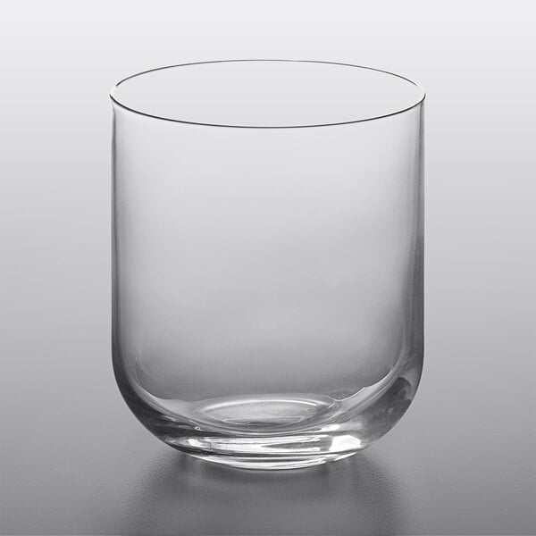 A Luigi Bormioli clear rocks glass with a curved bottom on a table.