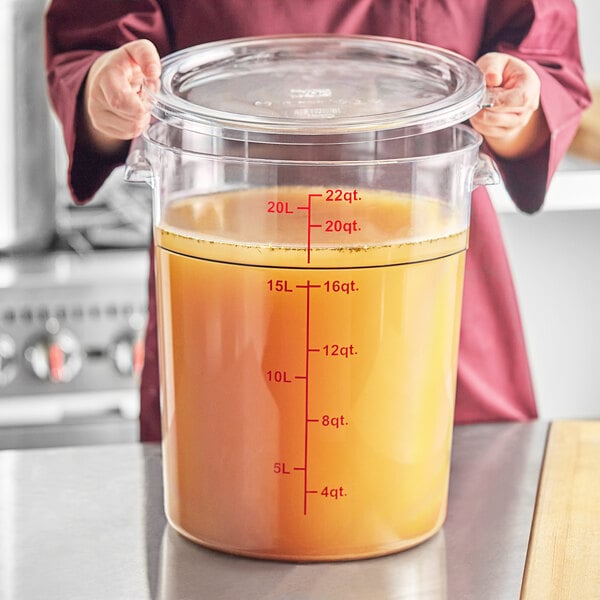 A woman holding a Choice clear round polycarbonate food storage container filled with liquid.