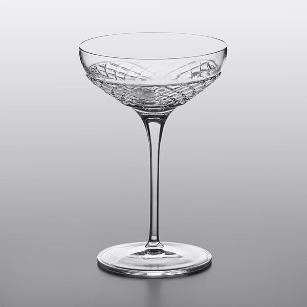 A Luigi Bormioli Roma coupe wine glass with a clear liquid, on a gray surface.