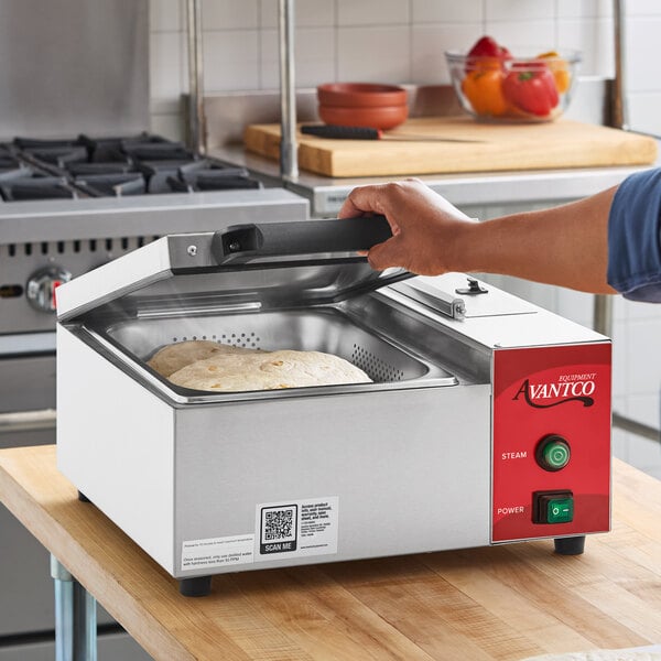 A stainless steel countertop tortilla and portion steamer with a red control panel, shown in use steaming tortillas.