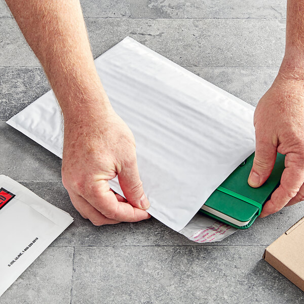 A person opening a white Lavex bubble mailer to reveal a green notebook.