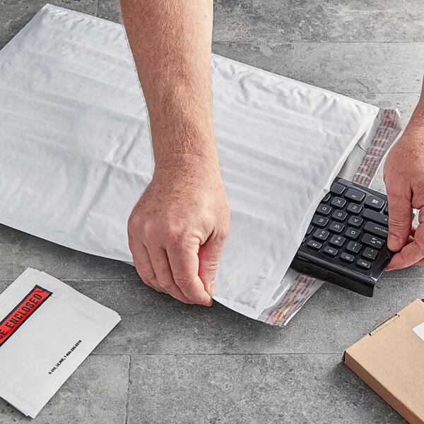 A person opening a white Lavex Self-Sealing Polyethylene Bubble Mailer with a keyboard.