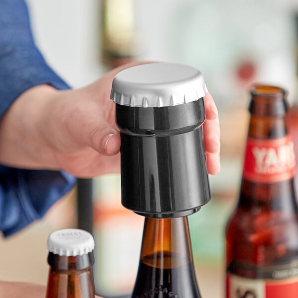 A person using a Franmara black Pop-Cap bottle opener to open a beer bottle.